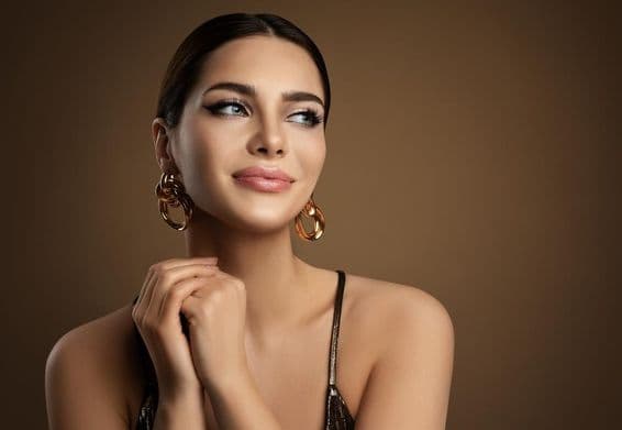 Mujer sonriente con piel tersa, maquillaje y pendientes de oro.