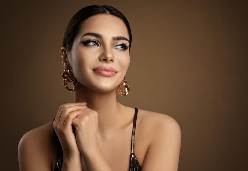 Mujer sonriente con piel tersa, maquillaje y pendientes de oro.