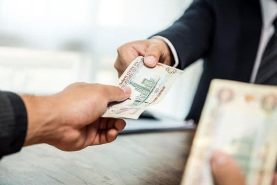 Empresario entregando dinero, dirhams, a otro empresario.