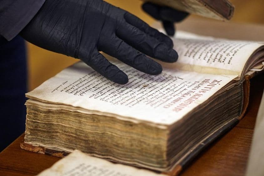 El bibliotecario con guantes sostiene un libro raro.