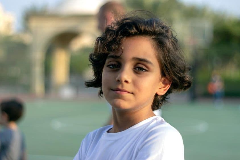 Un lindo niño pequeño de pie en una cancha de baloncesto y sonriendo.