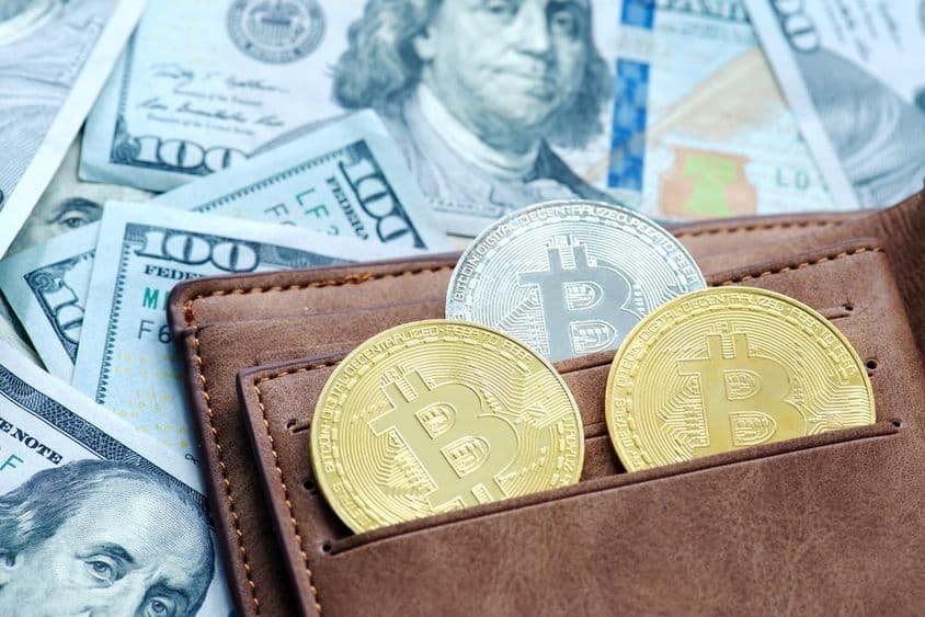 Bitcoin dorado con billetera, debajo de billetes de dólar.