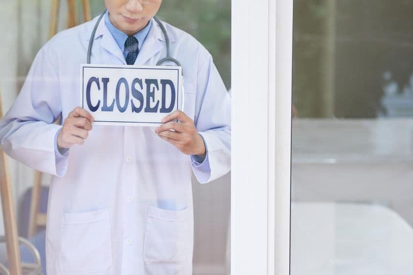 Un hombre en uniforme médico sosteniendo un cartel de cerrado.