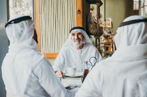 Tres hombres de negocios disfrutando de té en Dubái mientras visten prendas tradicionales emiratíes.