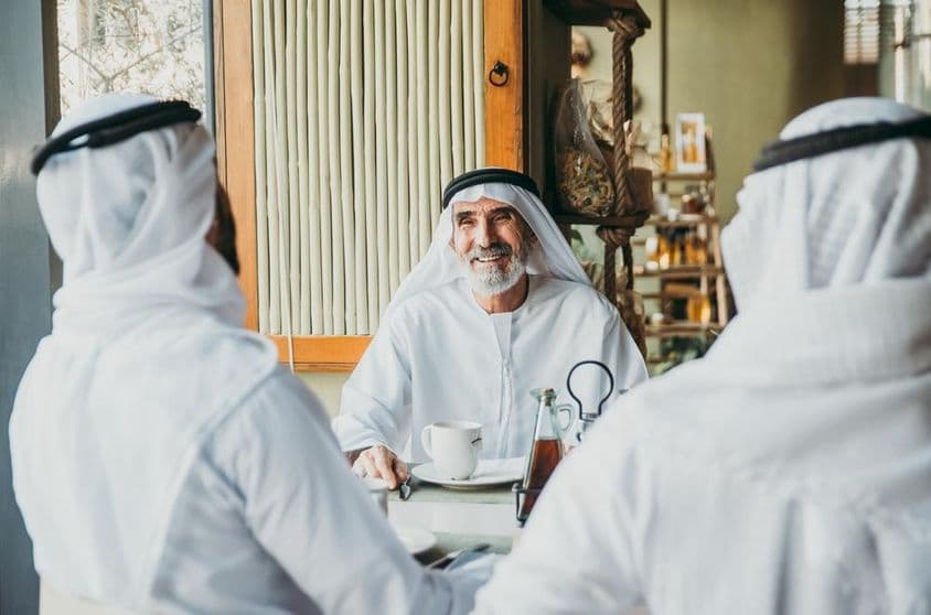 Tres hombres de negocios disfrutando de té en Dubái mientras visten prendas tradicionales emiratíes.