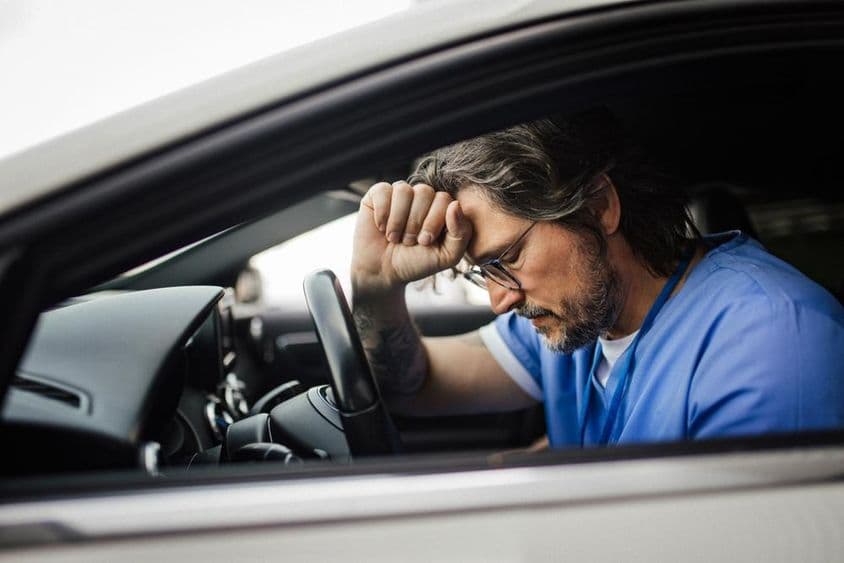 Médico en coche, exhausto.