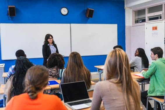 Estudiantes de secundaria escuchando a su maestro impartir una lección en un aula moderna.