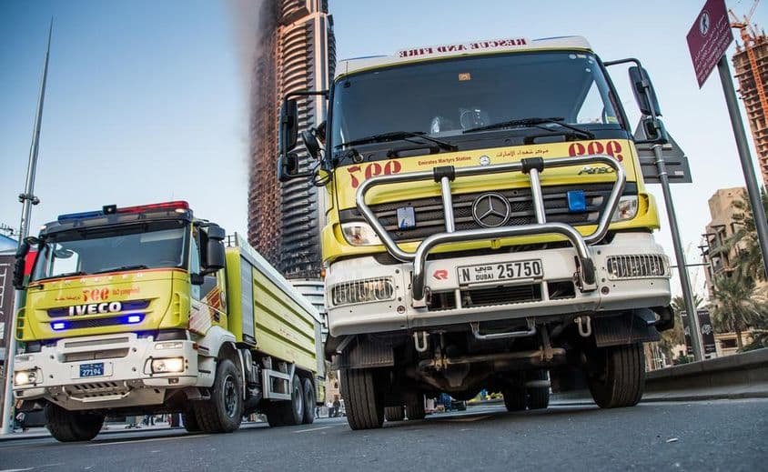 Camiones de bomberos de Dubái estacionados en las calles, edificio en llamas en el fondo.