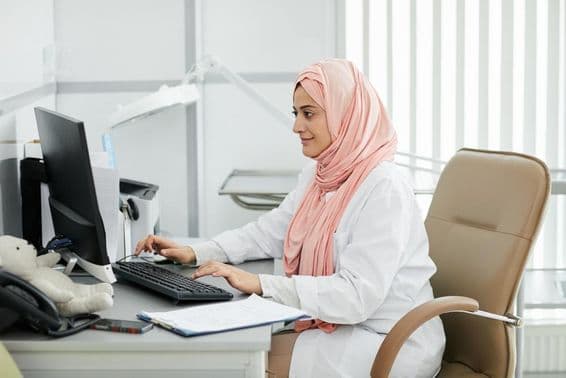 Una joven mujer de Oriente Medio usando un hijab trabajando como enfermera en una clínica médica.