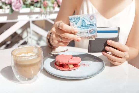 Chica pagando el desayuno en un café en Dubái con dirhams.