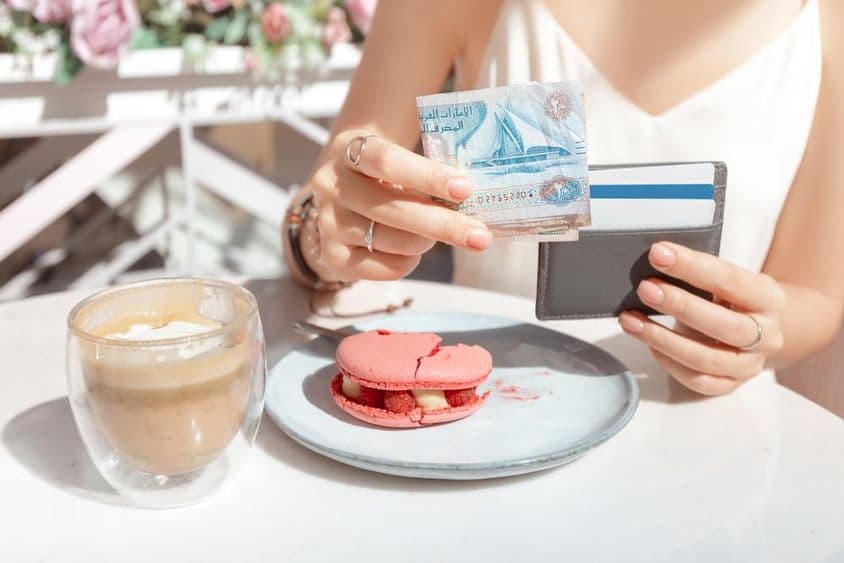 Chica pagando el desayuno en un café en Dubái con dirhams.
