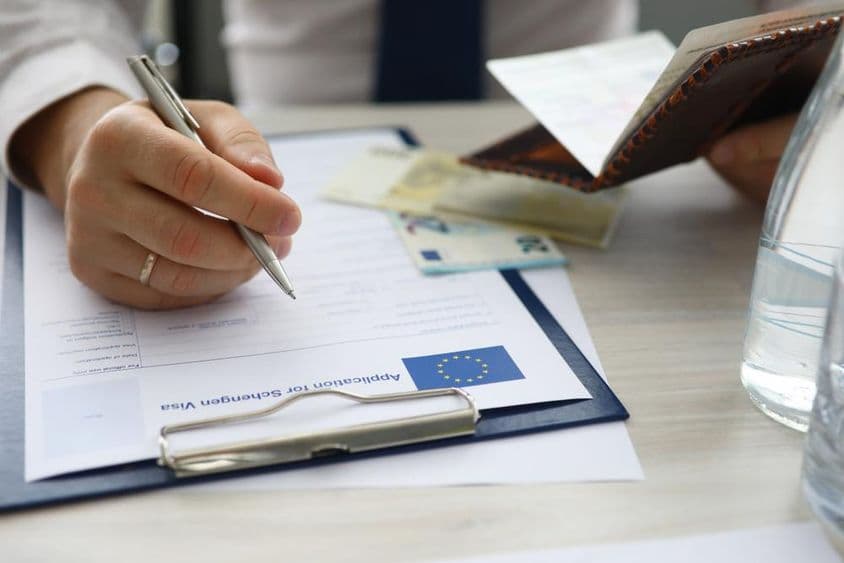 Un hombre sosteniendo un pasaporte e ingresando información personal en una aplicación de visa Schengen.