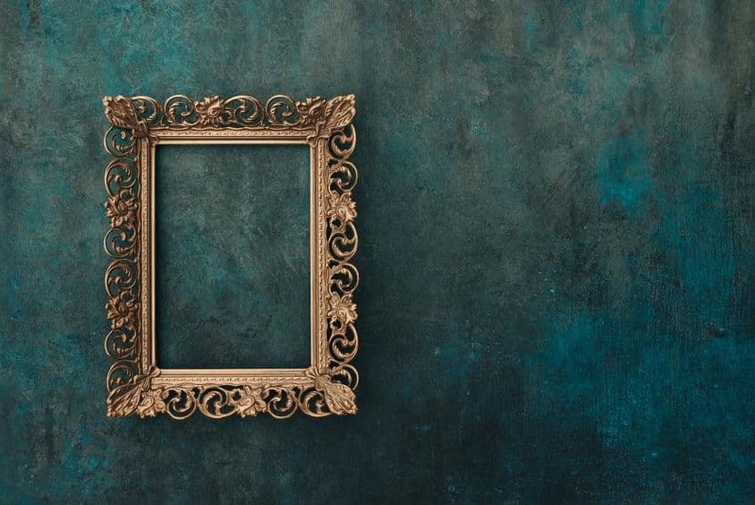 Marco vintage calado en metal bronce sobre una pared azul y verde envejecida.