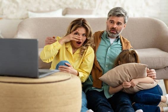 Padres de mediana edad y hija impactados viendo película en línea en una laptop.