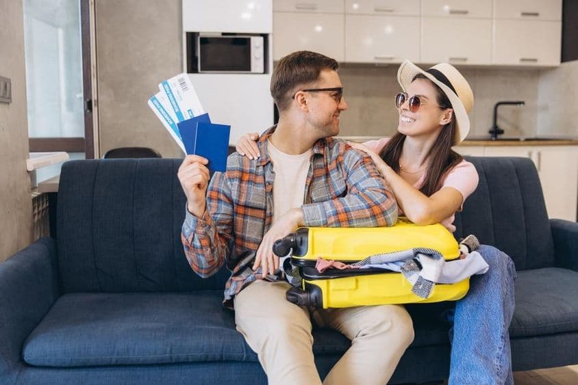 Pareja sonriente con pasaportes y tarjetas de embarque en mano, con una maleta.
