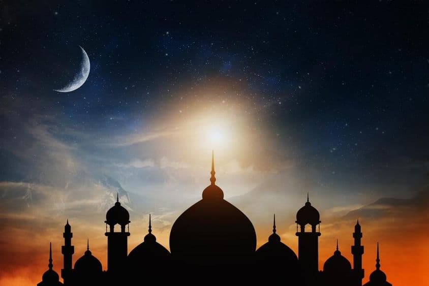 Cúpulas de mezquita contra un cielo crepuscular azul profundo con una luna creciente al fondo.