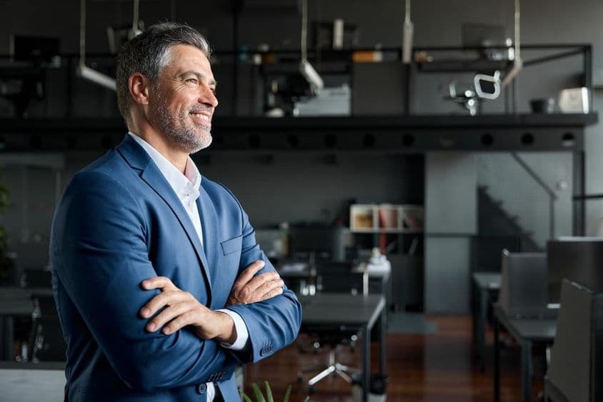 Empresario CEO en un traje de pie en una oficina con los brazos cruzados.