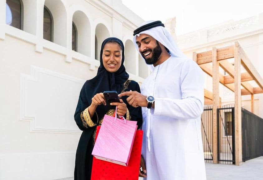 Pareja árabe tradicional con atuendo emiratí saliendo al aire libre.
