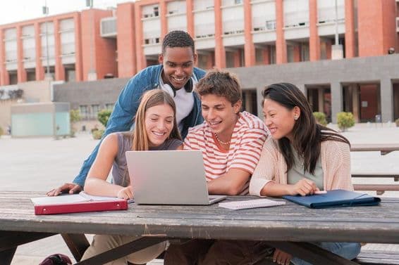 Un grupo de estudiantes utilizando una computadora portátil mientras busca información para un proyecto al aire libre.