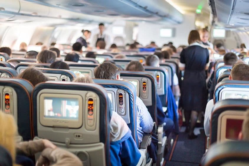 Interior de un avión con personas, asientos y auxiliares de vuelo.