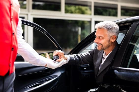 Empresario entrega llaves del coche al valet en estacionamiento de hotel.