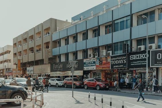 Calle concurrida en Bur Dubai con tiendas de joyas, peatones y automóviles en un día soleado.