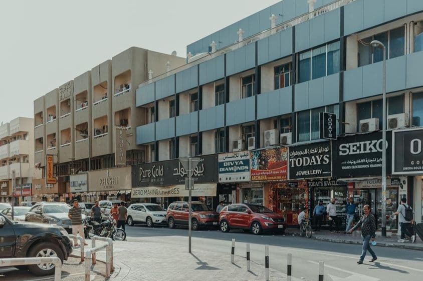 Calle concurrida en Bur Dubai con tiendas de joyas, peatones y automóviles en un día soleado.