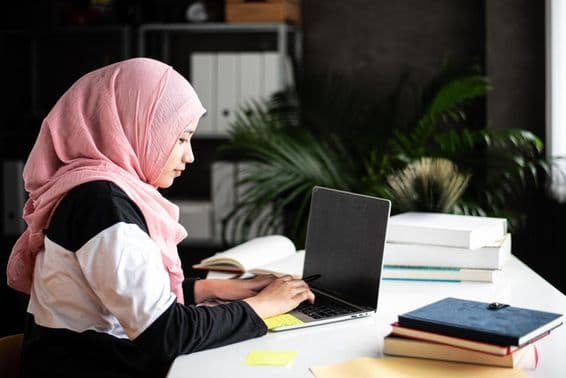 Una hermosa mujer musulmana estudia en casa usando una computadora portátil.