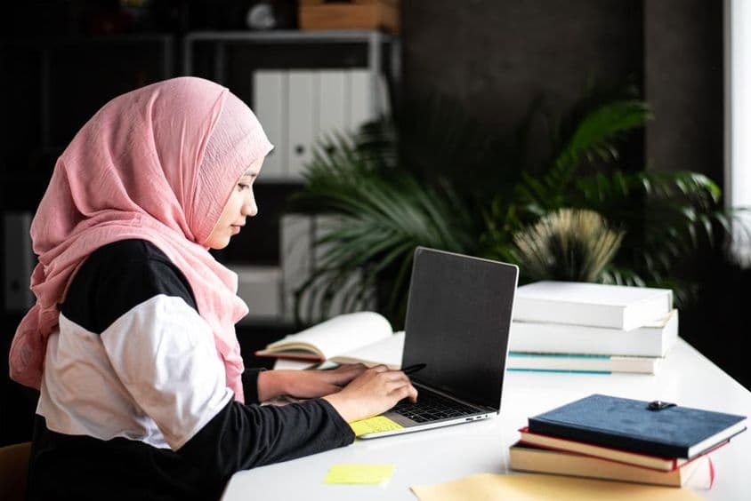 Una hermosa mujer musulmana estudia en casa usando una computadora portátil.