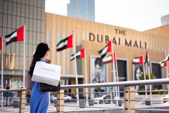 Turista asiático con bolsas de compras en la entrada principal de Dubai Mall.