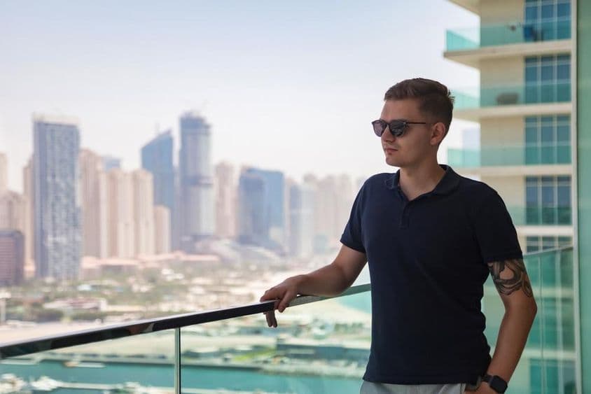 Un joven con gafas de sol de pie en el balcón de un rascacielos con vista a Dubái.