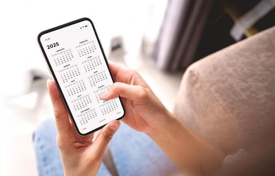 Mujer de negocios planeando actividades de 2025 con smartphone y calendario mensual.