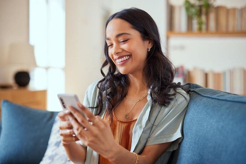 Mujer Latina alegre usando un teléfono inteligente.