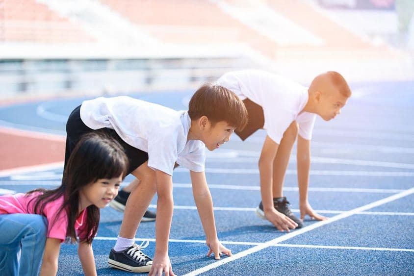 Niños preparándose para una carrera en una pista azul.