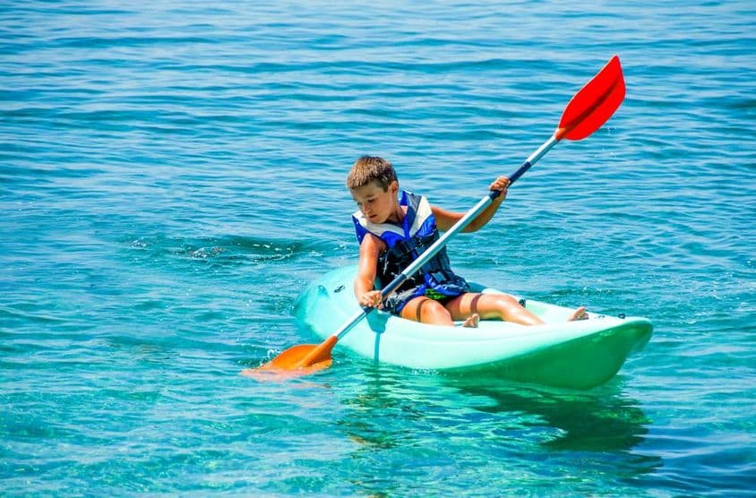 Niño con boya de salvavidas durante lecciones de kayak en vacaciones de verano.