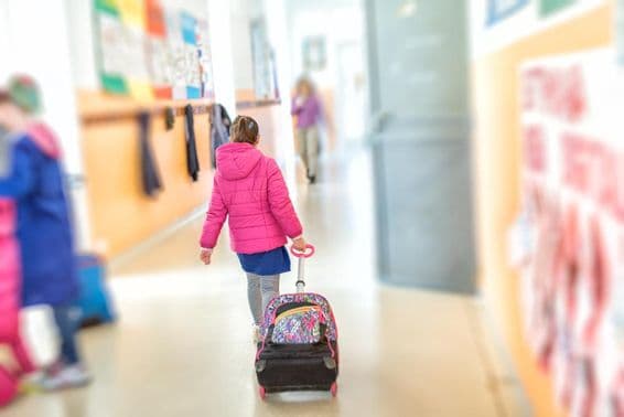 Una niña joven tira de una mochila escolar con ruedas.