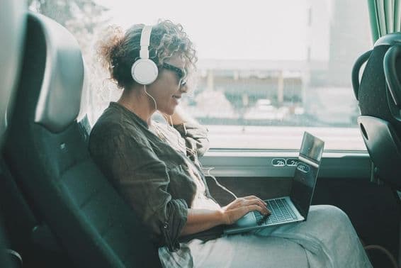 Joven trabajando en un portátil con auriculares en un asiento de autobús.