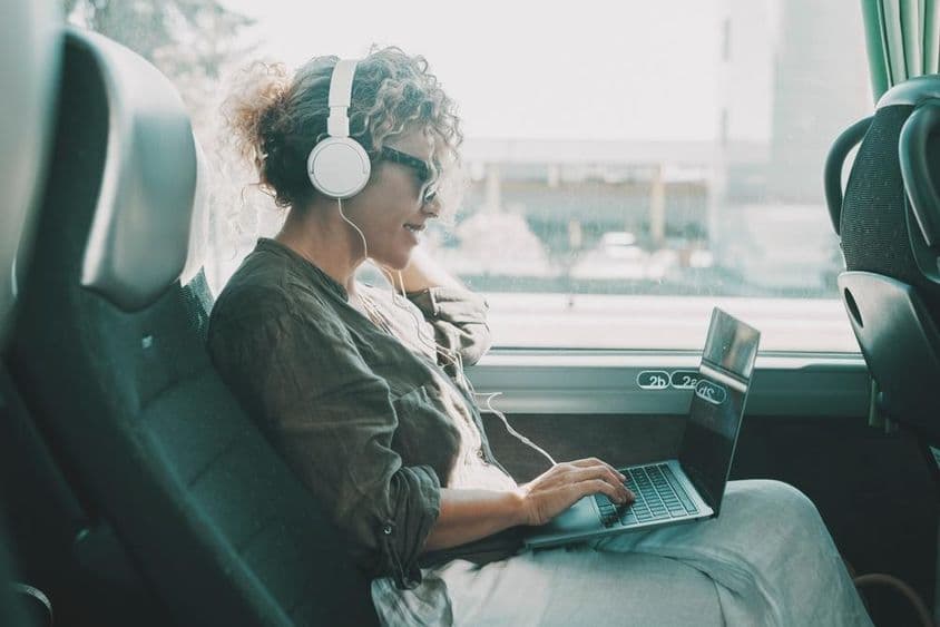 Joven trabajando en un portátil con auriculares en un asiento de autobús.