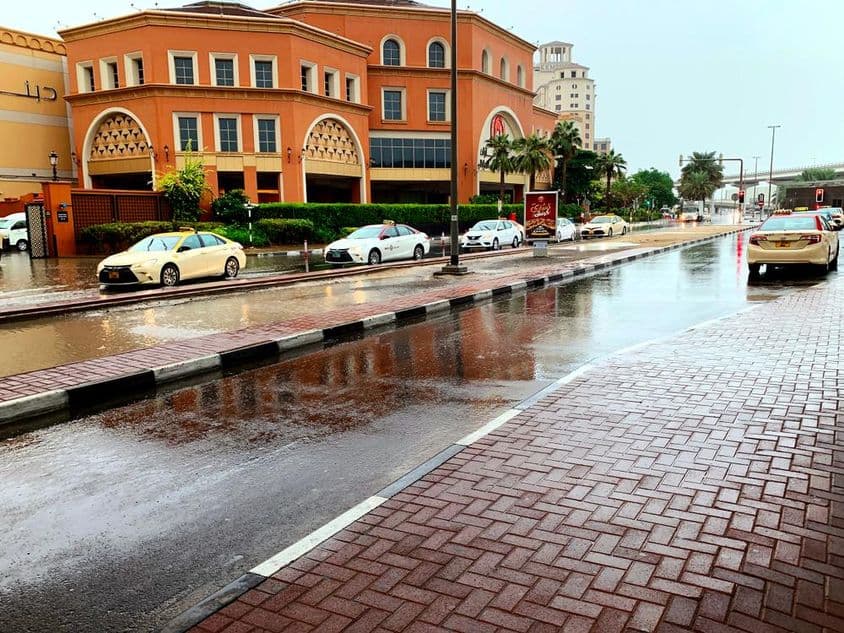 Coches conduciendo por calles inundadas de Dubai bajo la lluvia.