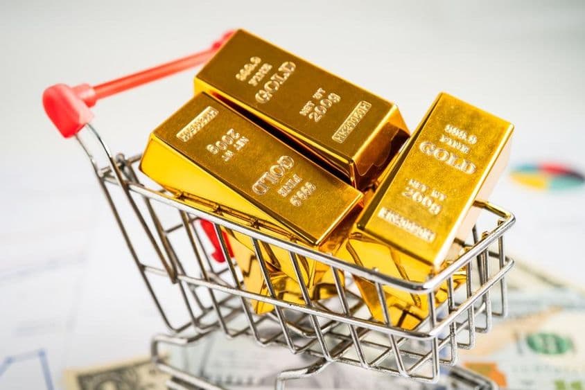 Barra de oro en un carrito de compras sobre billetes de dólar estadounidenses.