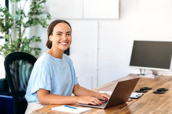 Mujer segura sentada en un escritorio moderno, mirando a la cámara y sonriendo amigablemente.