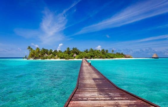 Muelle sobre océano azul que lleva a una playa tropical de isla, Maldivas.