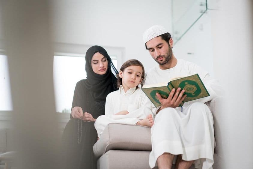 Padres jóvenes y un pequeño niño leyendo de un libro.