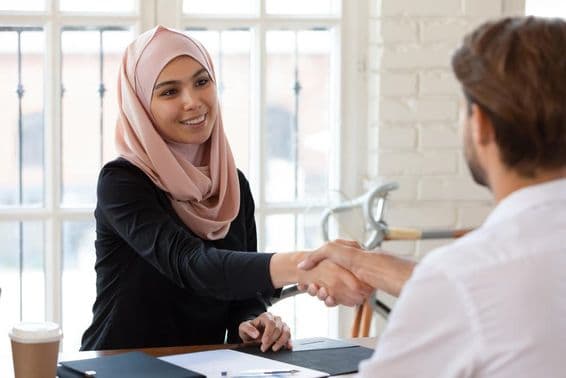 Gerente de recursos humanos árabe con hijab dándole la mano a un solicitante masculino.