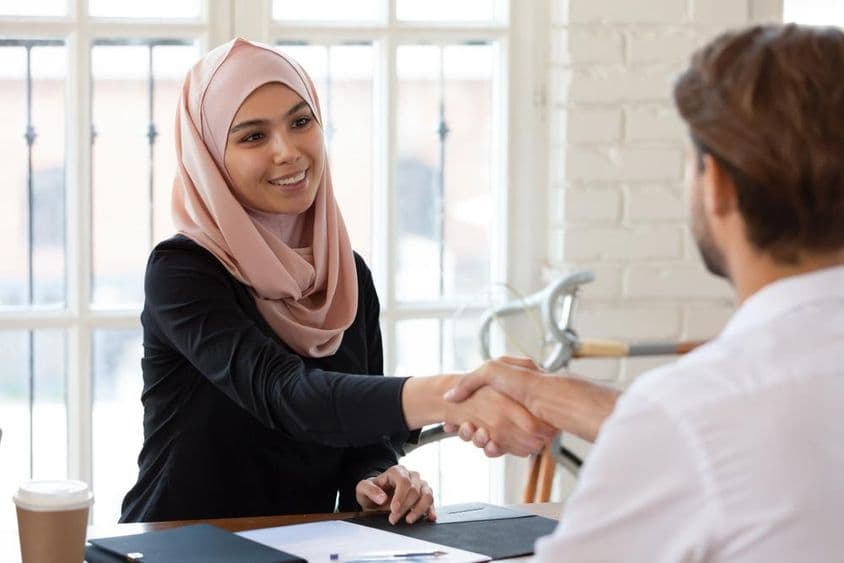 Gerente de recursos humanos árabe con hijab dándole la mano a un solicitante masculino.