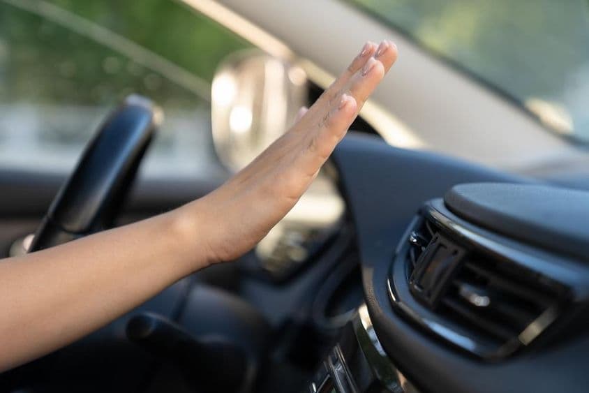 La mano de una mujer comprueba el panel del aire acondicionado en un coche.