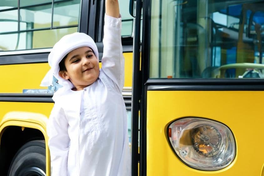 Estudiante de escuela primaria árabe cerca de un autobús escolar amarillo.