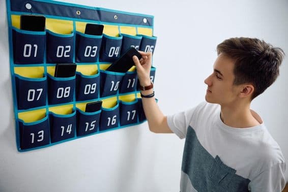 Estudiante deja un smartphone en un organizador de teléfonos montado en la pared.