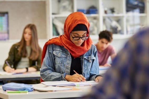 Estudiante femenina joven estudiando con un hijab mientras toma notas.