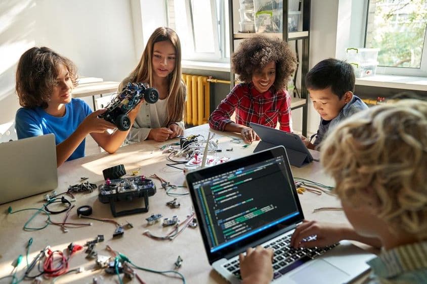 Escolares construyendo coches robóticos usando computadoras y programación.